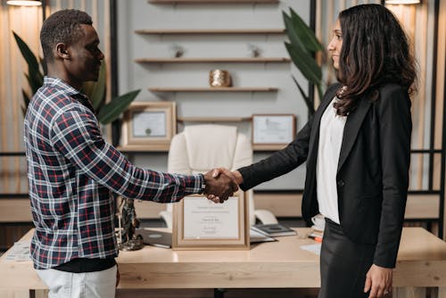 Man in Blue and White Plaid Up Button Shirt Shaking Hands With Woman in Black Blazer 