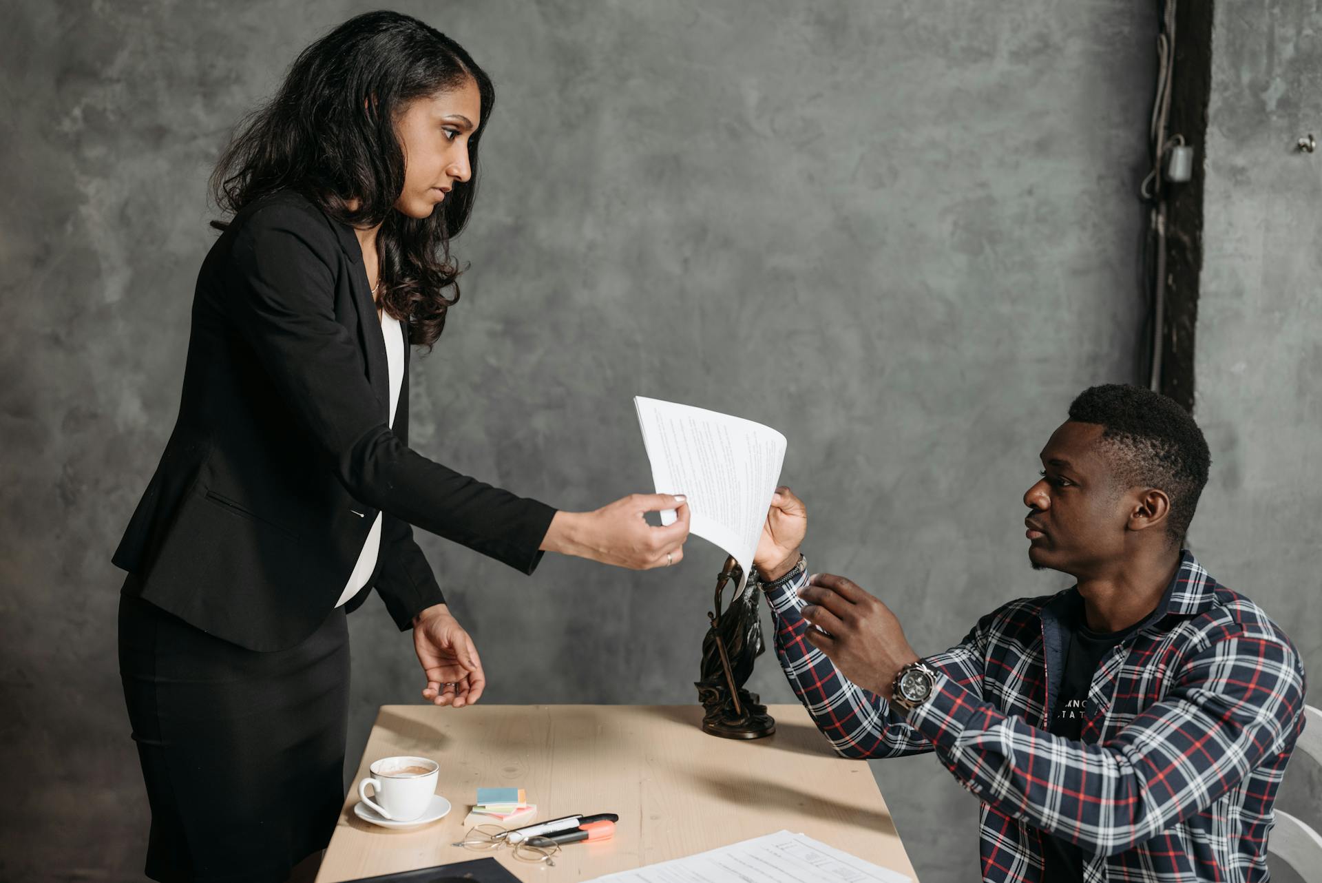 Professional setting with lawyer handing contract to client across table.