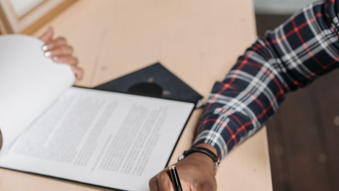 Hands of a person signing official documents on a desk in an office setting.