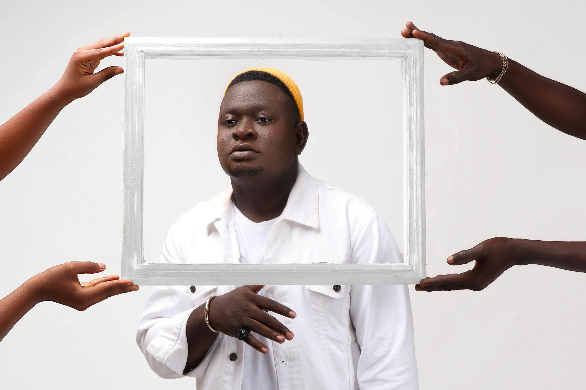 Artistic portrait of a man in white, framed by four hands against a white background.