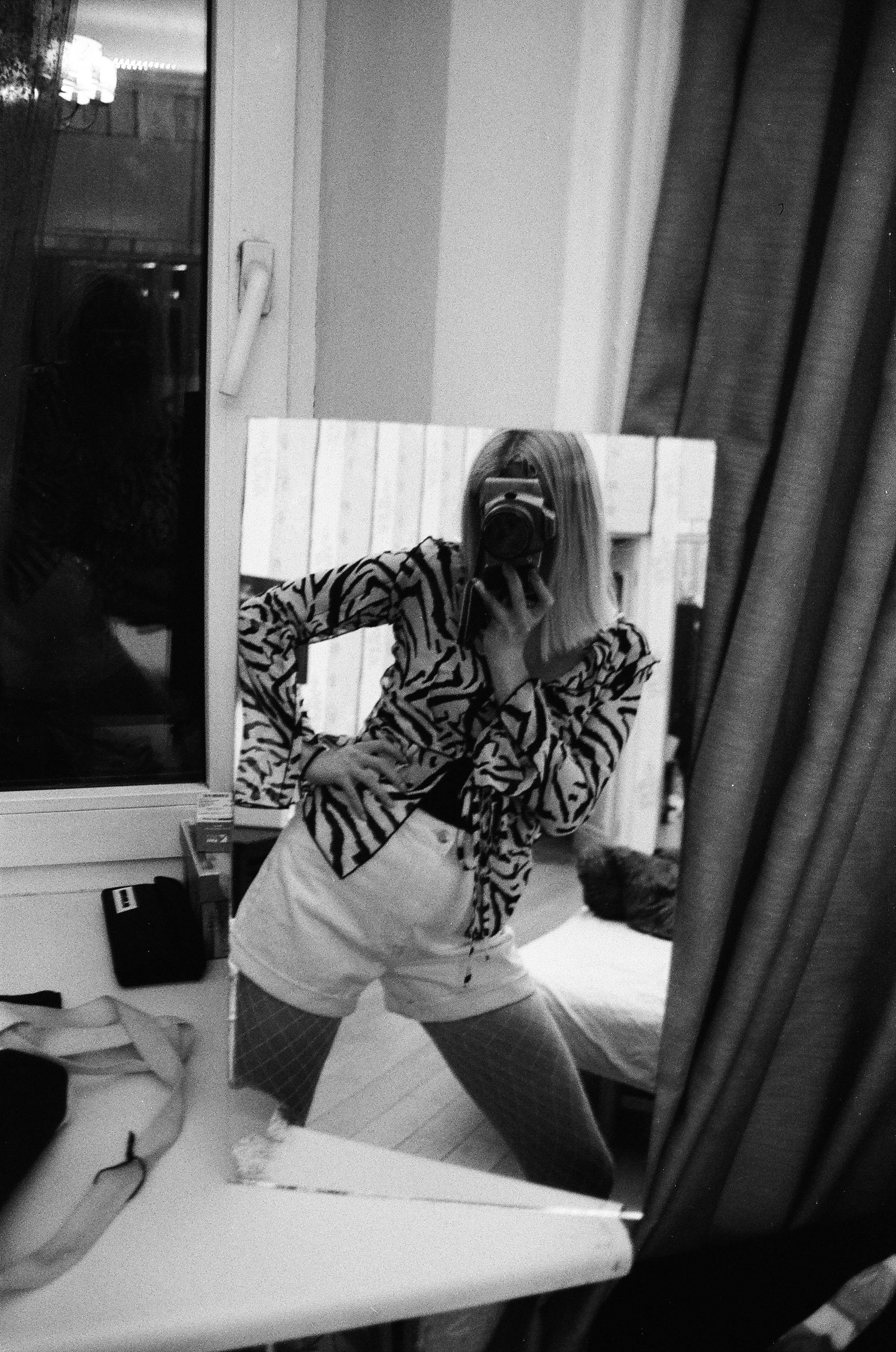Monochrome photo of a woman posing in front of a mirror capturing a candid reflection.