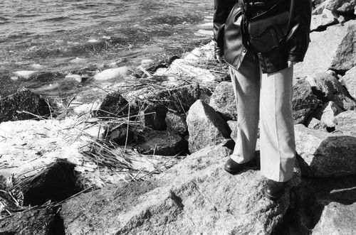 Free Black and white image of a person standing on coastal rocks by the sea wearing trousers. Stock Photo