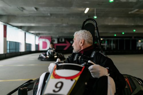 Free Senior man driving a go-kart indoors, showcasing the excitement of kart racing. Stock Photo