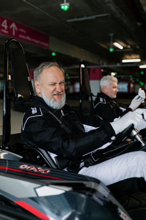 Free Elderly men wearing race suits smile while driving go-karts indoors, enjoying leisure and friendship. Stock Photo