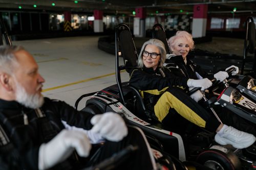 Free Three senior adults in racing suits enjoying indoor go-karting together. Stock Photo