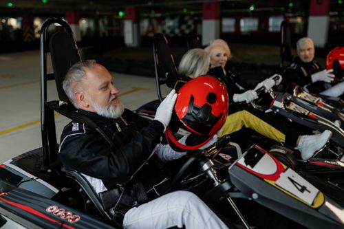 Free Senior adults prepare for an exciting indoor go-kart race, highlighting adventure and leisure. Stock Photo