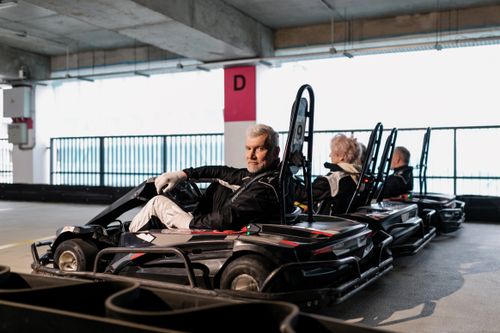 Free Elderly men and women participate in a thrilling indoor go-kart race. Stock Photo