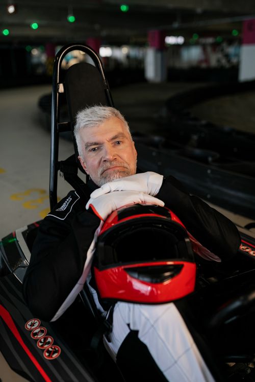 Free Elderly man in racing suit resting in a go-kart with a helmet indoors. Stock Photo