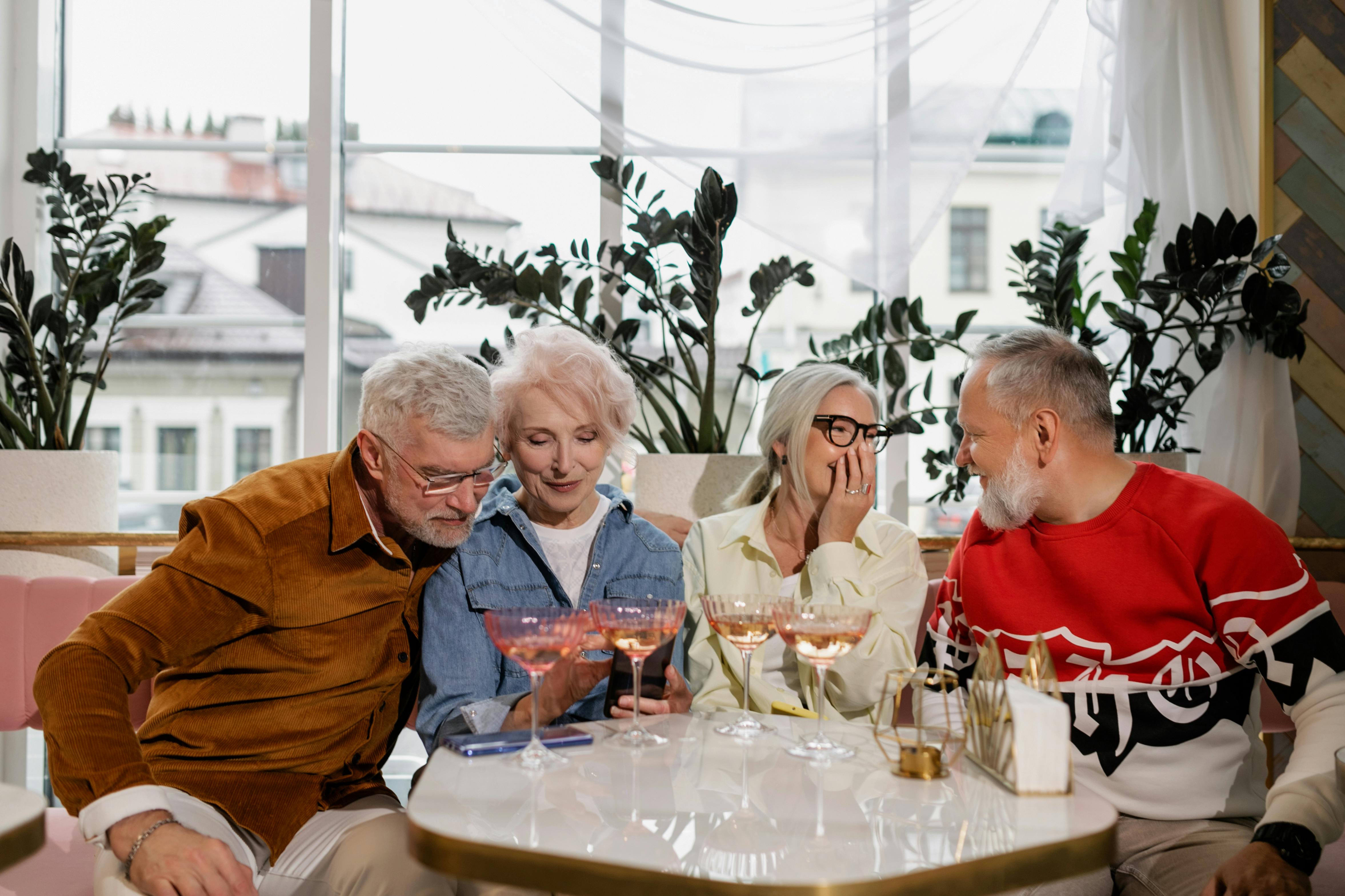 Senior friends enjoy a cheerful gathering with drinks in a cozy indoor setting.