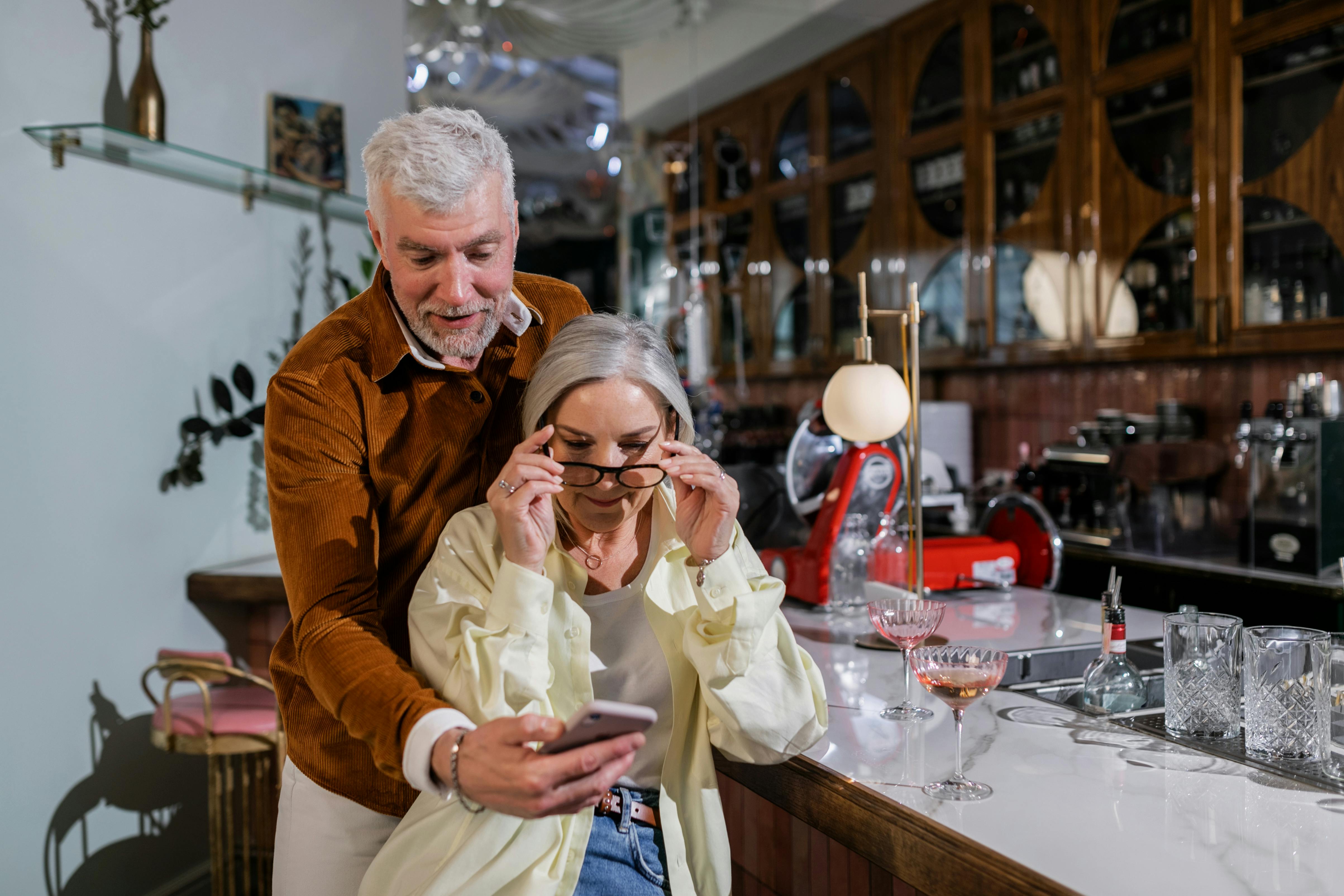 Elderly couple sharing a joyful moment while using a smartphone at a cozy bar.