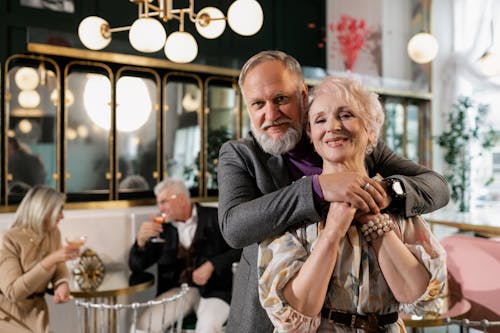 Senior couple embracing happily at a cozy indoor cafe, radiating love and warmth.