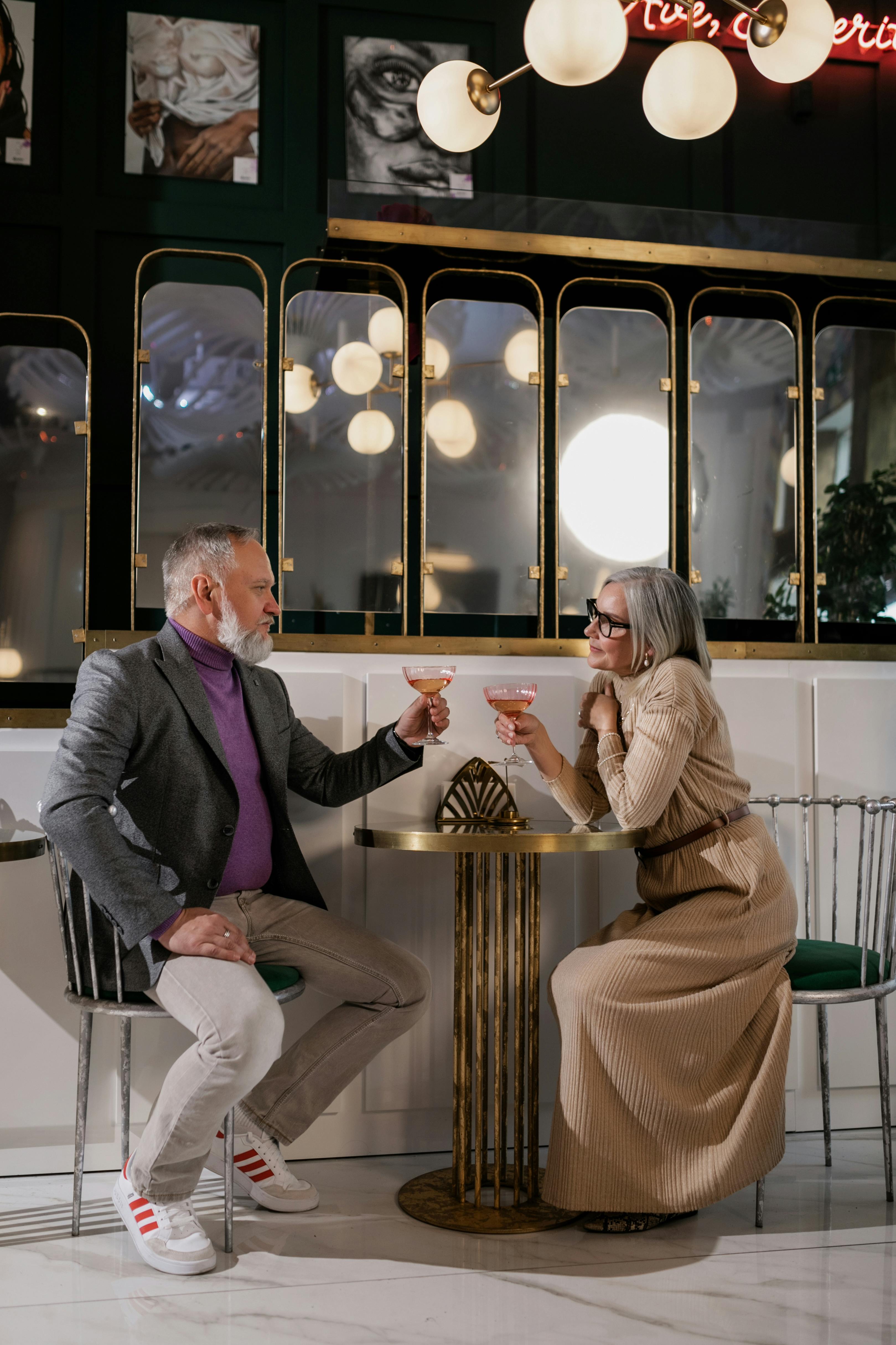 Sophisticated elderly couple enjoying a toast in a chic indoor cafe setting.