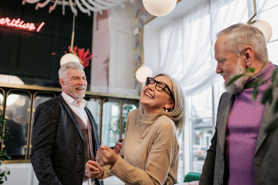 Three senior adults laughing and enjoying a lively indoor gathering, creating a joyful atmosphere.