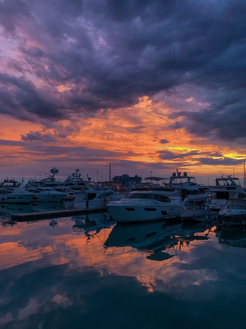 Free Vibrant sunset over a marina, highlighting docked yachts and colorful clouds reflecting on calm waters. Stock Photo