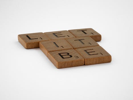 Close-up of wooden Scrabble tiles spelling 'Let It Be' on a white background.