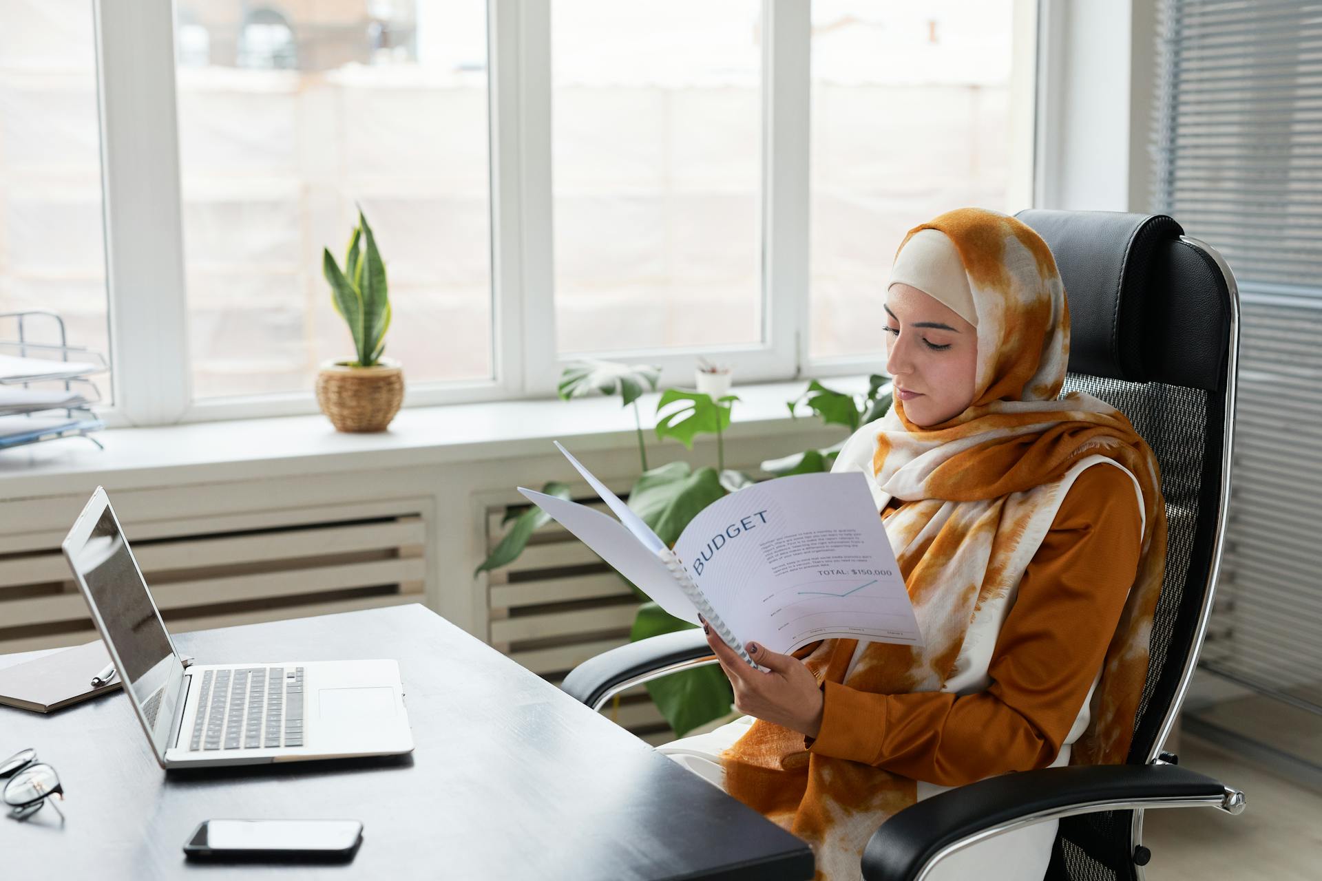 Muslim businesswoman in hijab working on budget documents at office desk.