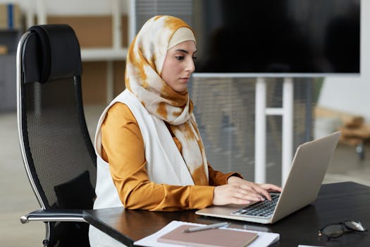 Professional Muslim woman in headscarf working on laptop at office desk.
