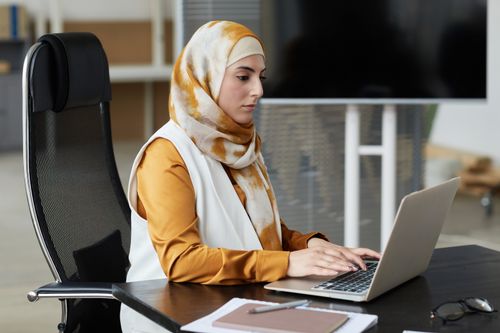 Free Professional Muslim woman in headscarf working on laptop at office desk. Stock Photo