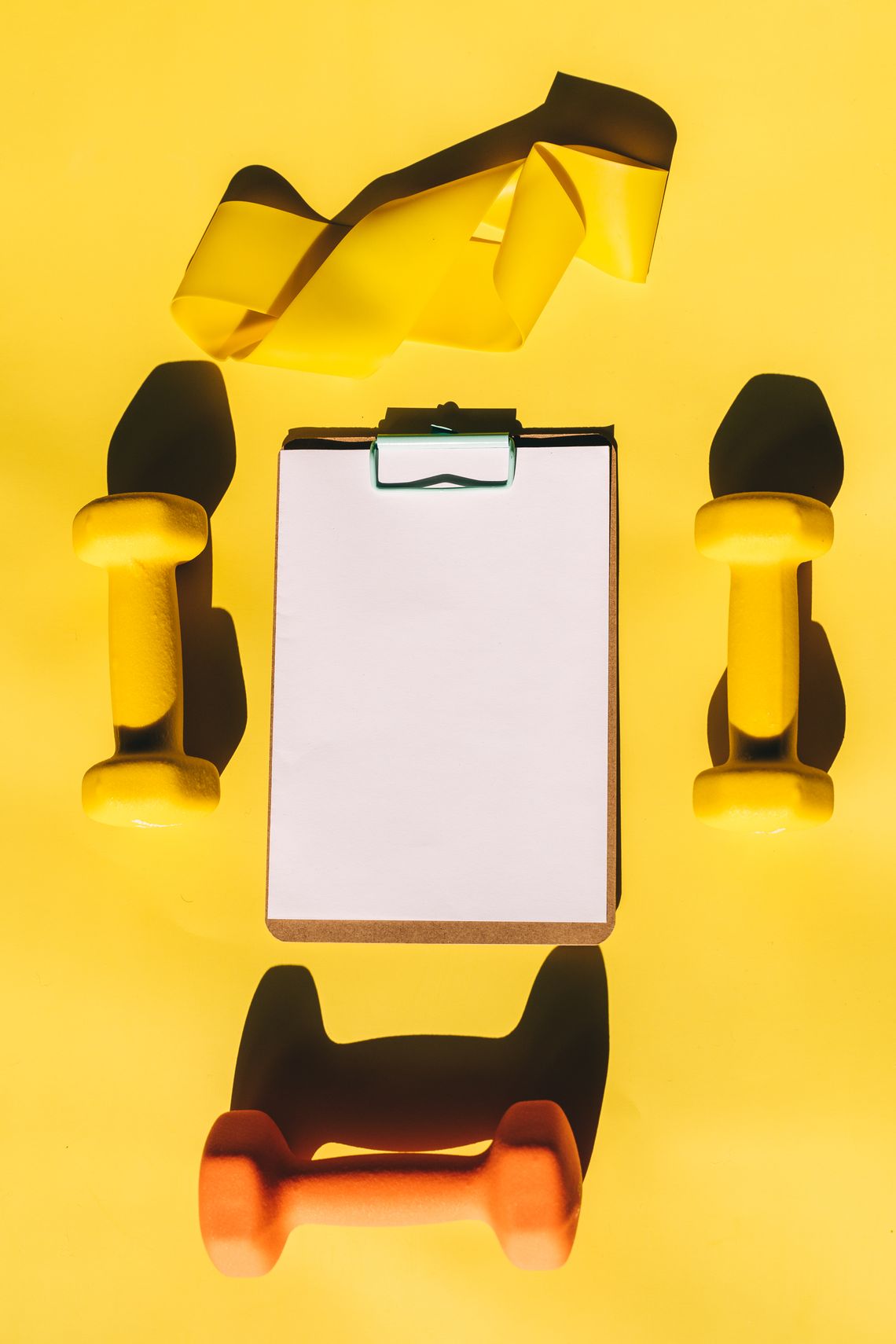 Real fitness planning setup with dumbbells, training accessories, paper and clipboard