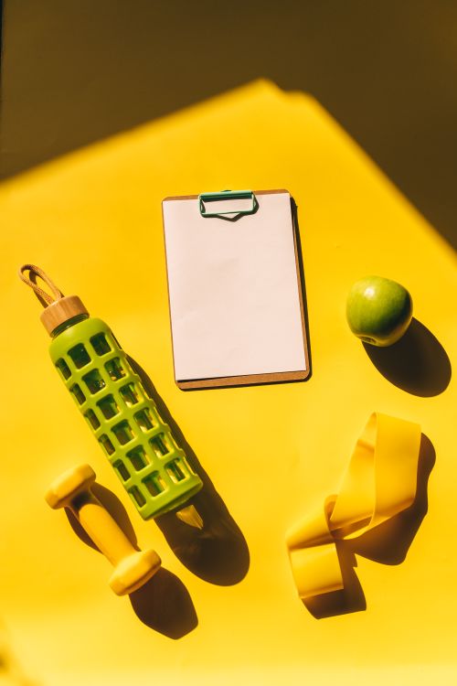 Free Bright flat lay of fitness essentials including dumbbells, water bottle, and apple on a yellow background. Stock Photo