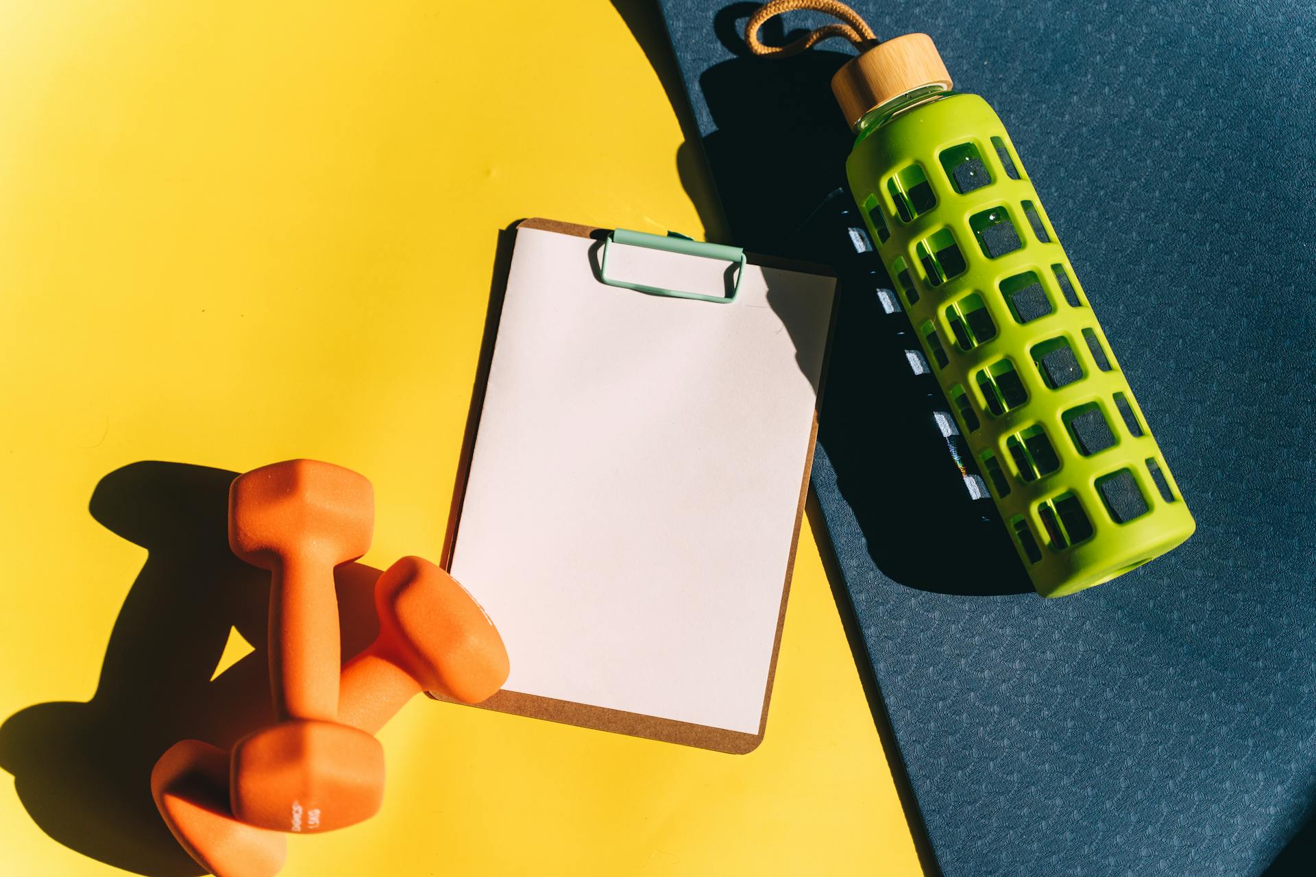 Brightly colored dumbbells, clipboard, and water bottle on a vibrant yellow background.