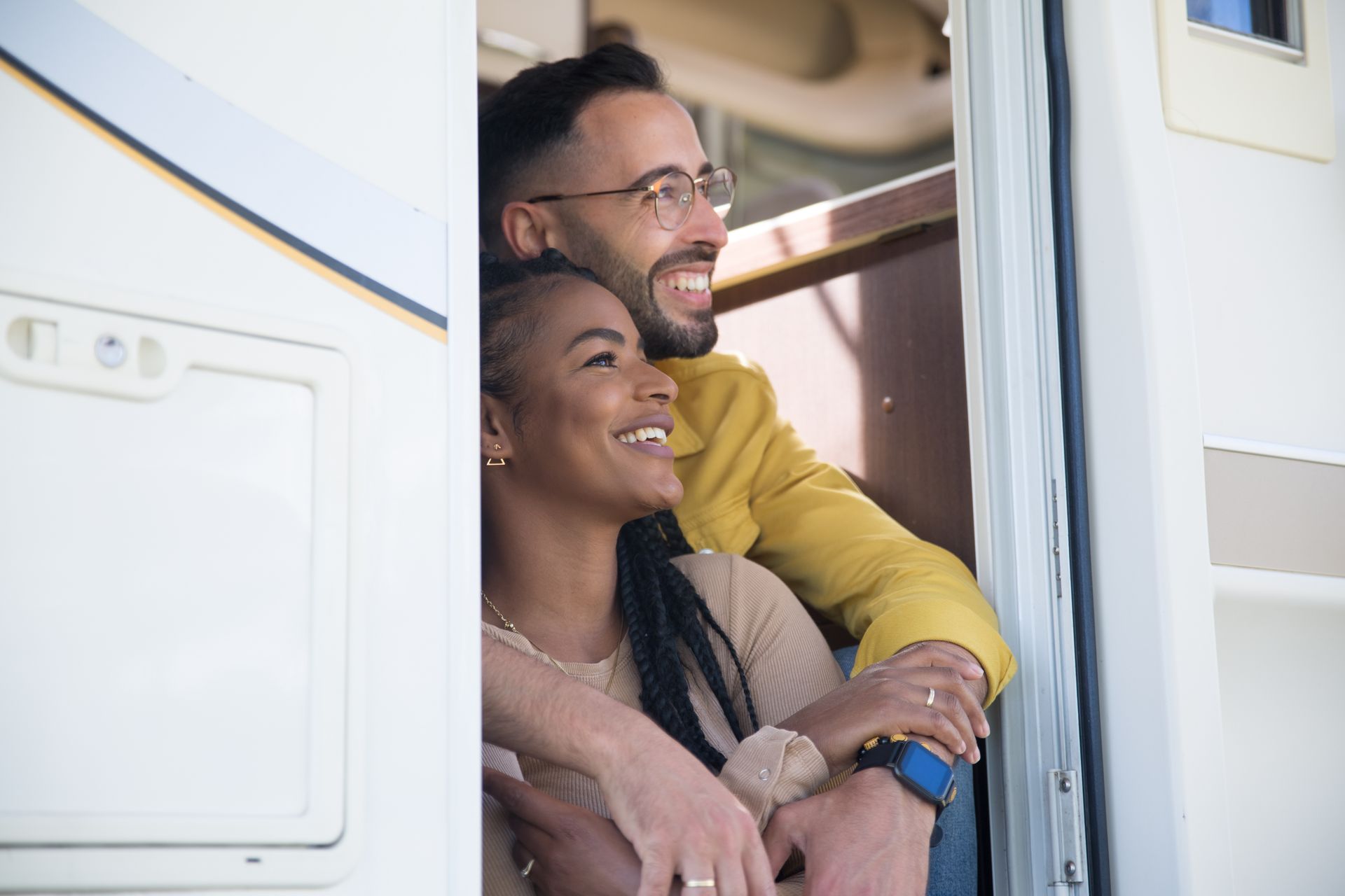 A joyful couple enjoys a moment together sitting in their RV doorway, exuding love and happiness.