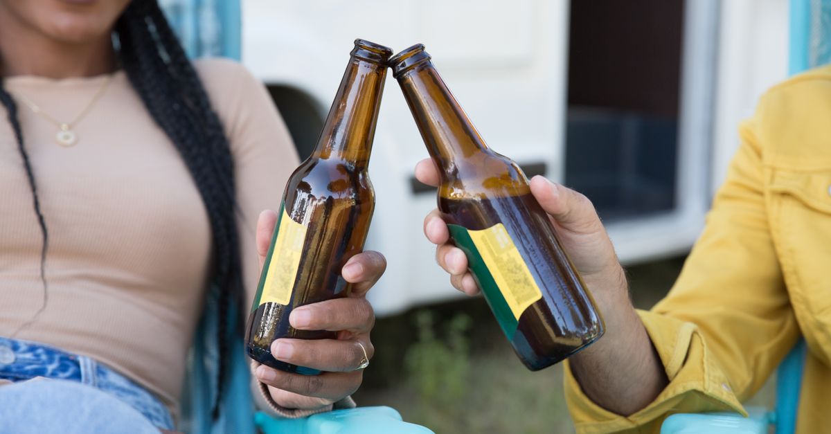 person clinking beer glasses with a friend while checking a phone showing a savings account balance