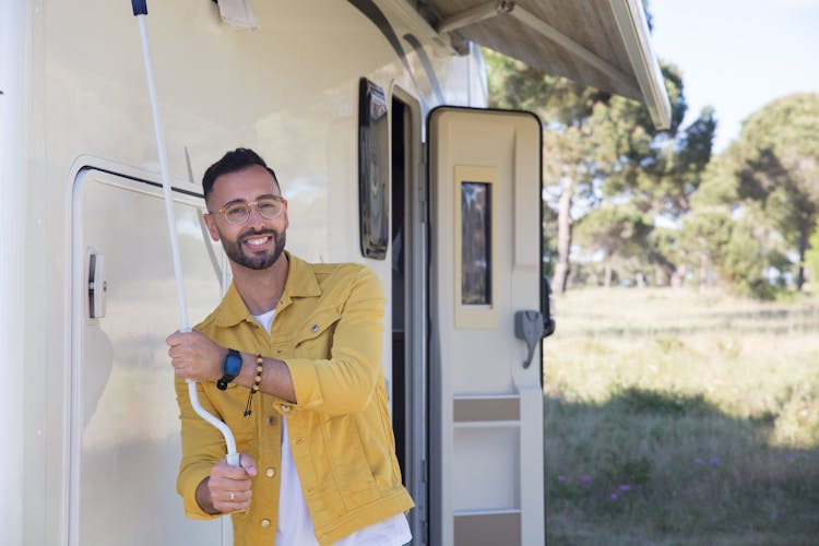 Smiling Man In Yellow Jacket Standing Near The Door Of A Camper Van