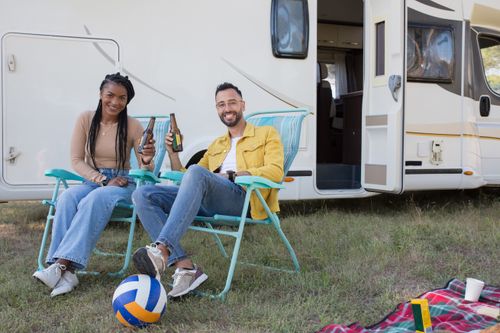 Free Smiling couple enjoying a camping trip with beer near a caravan in Portugal. Stock Photo