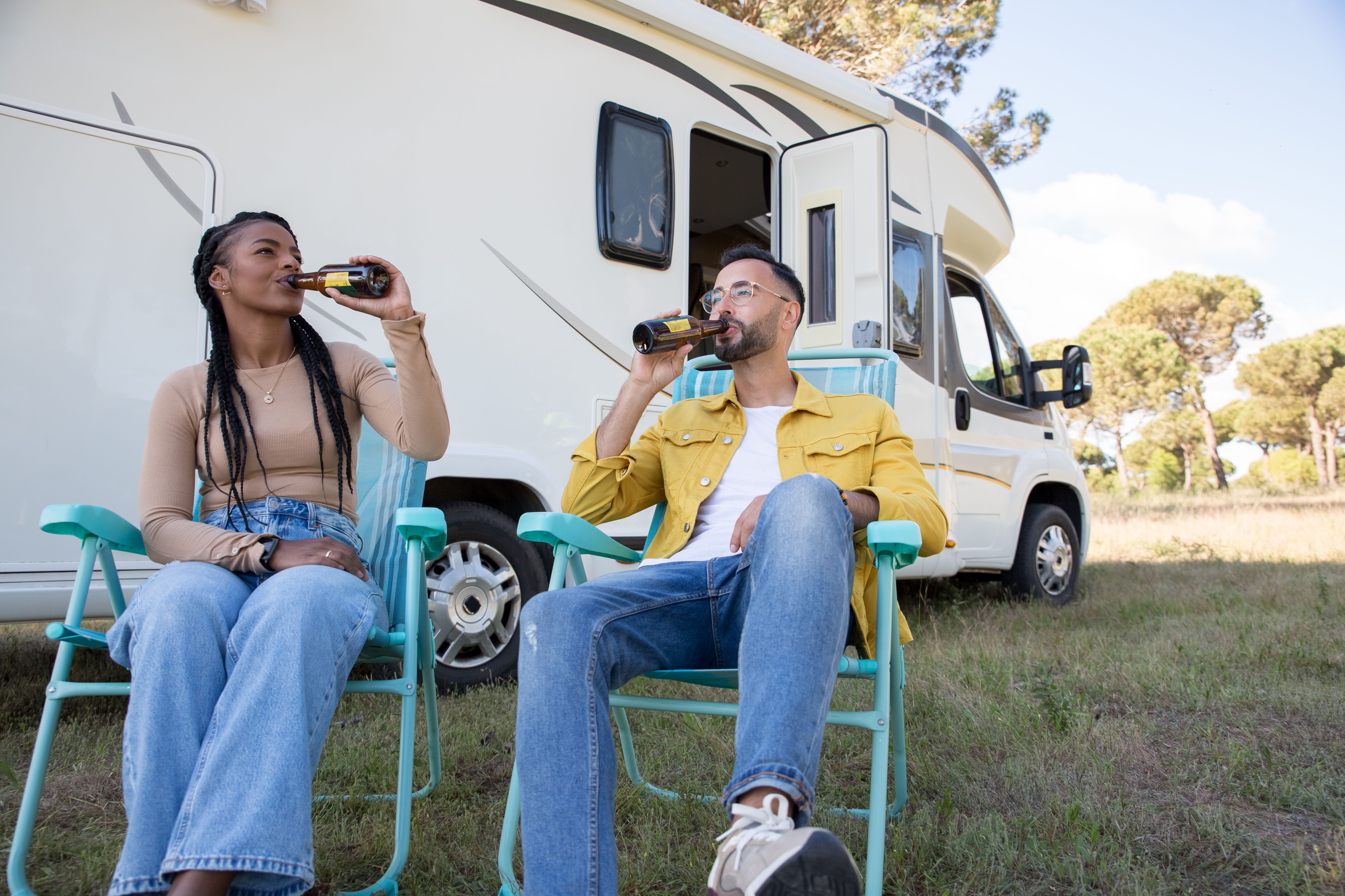 Couple sitting in front of campervan drinking, enjoying outdoor leisure time in Portugal.