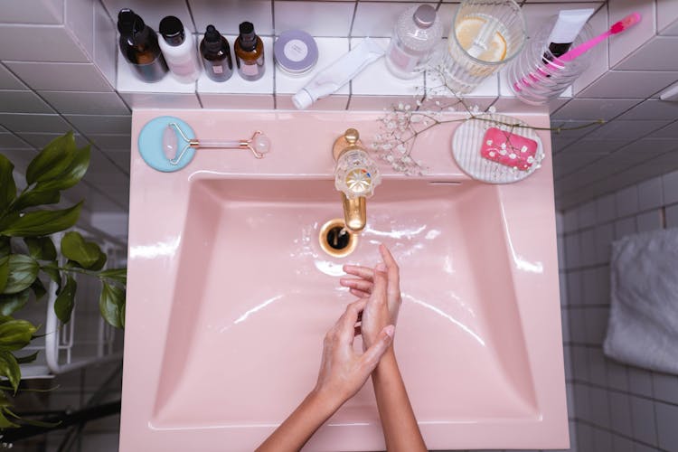 Person Washing Hands On Pink Ceramic Sink