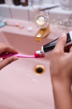 Close-up of a person applying toothpaste to a toothbrush in a stylish pink bathroom.