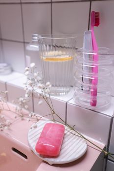 A clean and modern bathroom setup featuring a pink toothbrush, soap, and refreshing drink.