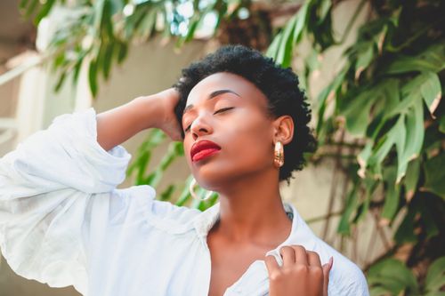 Free Stylish African woman in a serene outdoor pose with eyes closed and vibrant red lips. Stock Photo