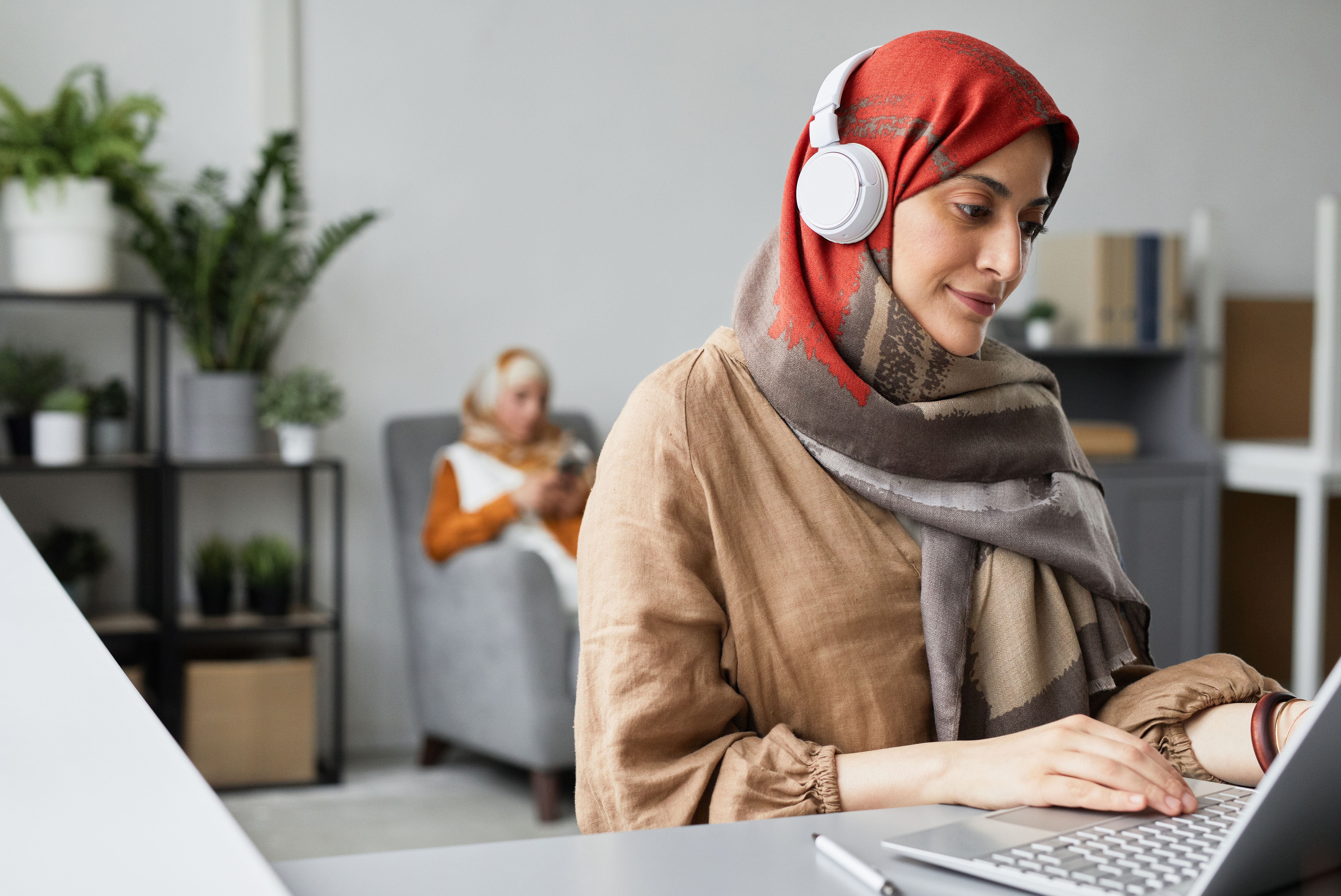 Woman in Hijab Wearing Headphones while Using a Laptop · Free Stock Photo