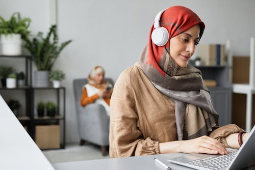 Woman in Hijab Wearing Headphones while Using a Laptop