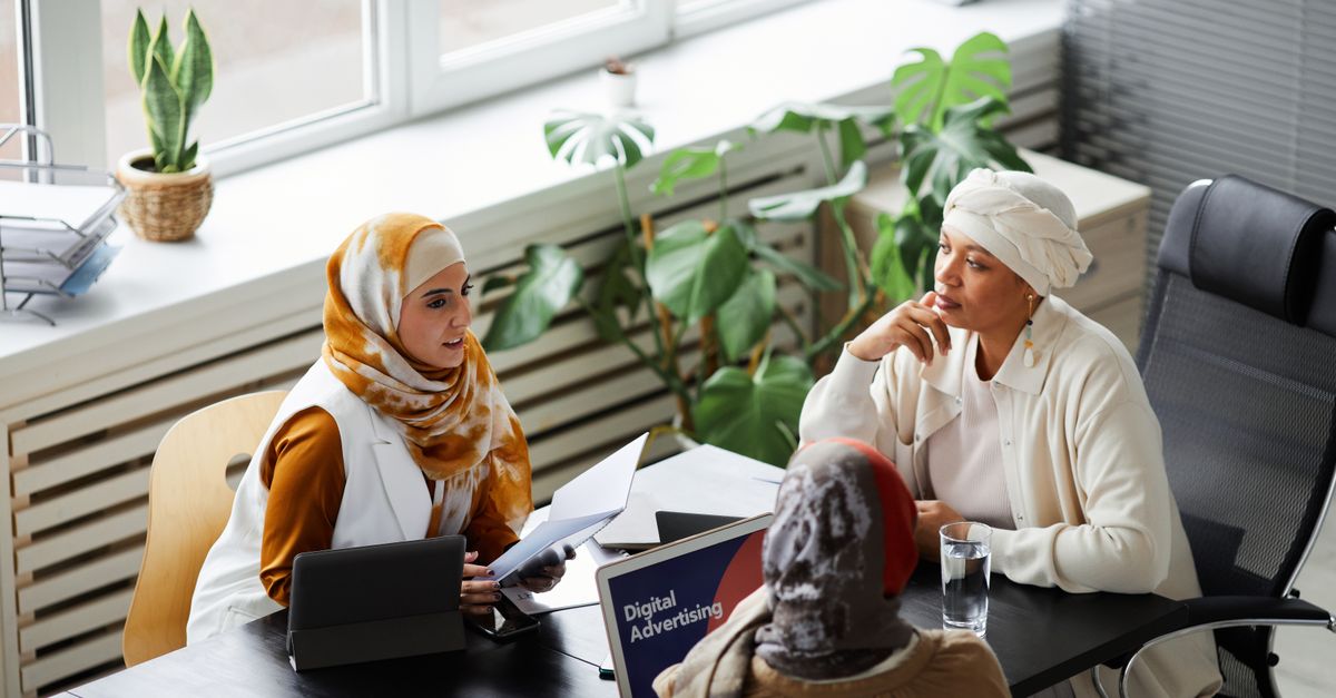 Three diverse women in hijabs discussing digital advertising strategy in a bright modern office.