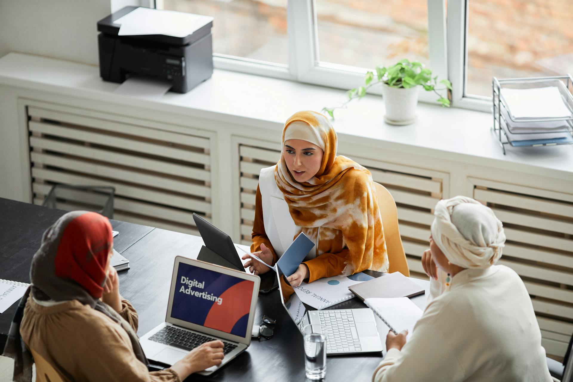 Three businesswomen in hijabs discussing digital advertising at an office table.