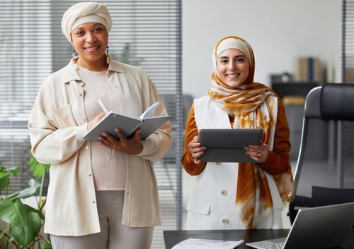 Free Two smiling businesswomen in hijabs collaborating with notes and tablet in modern office. Stock Photo