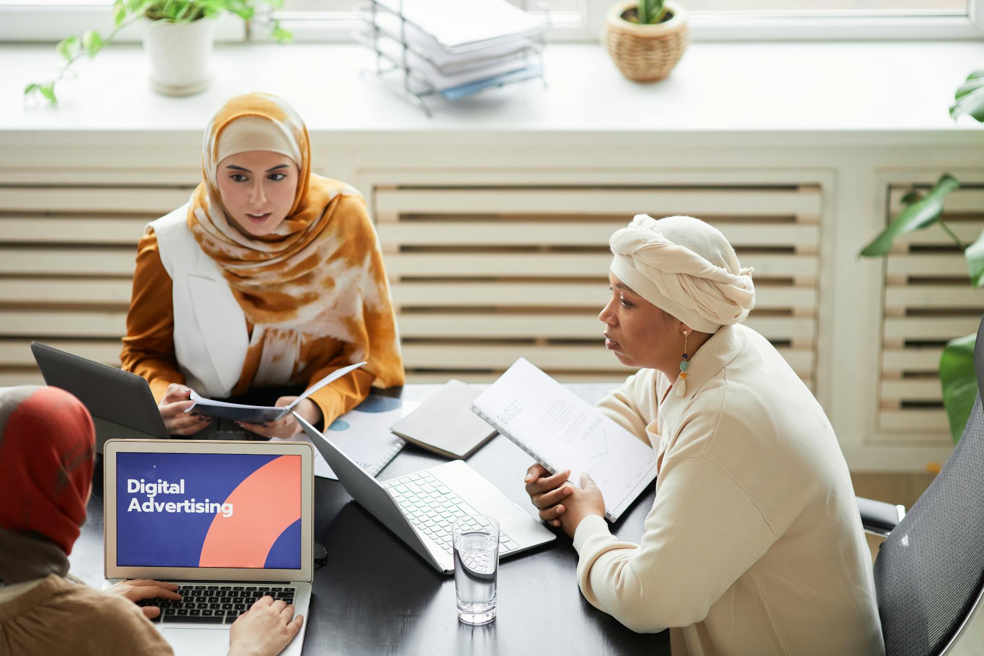 Three women in hijabs collaborating on digital advertising strategies around a table with laptops.