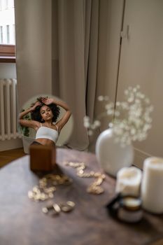 Young woman in white tube top reflected in a mirror during morning routine, in a stylish bedroom setting.