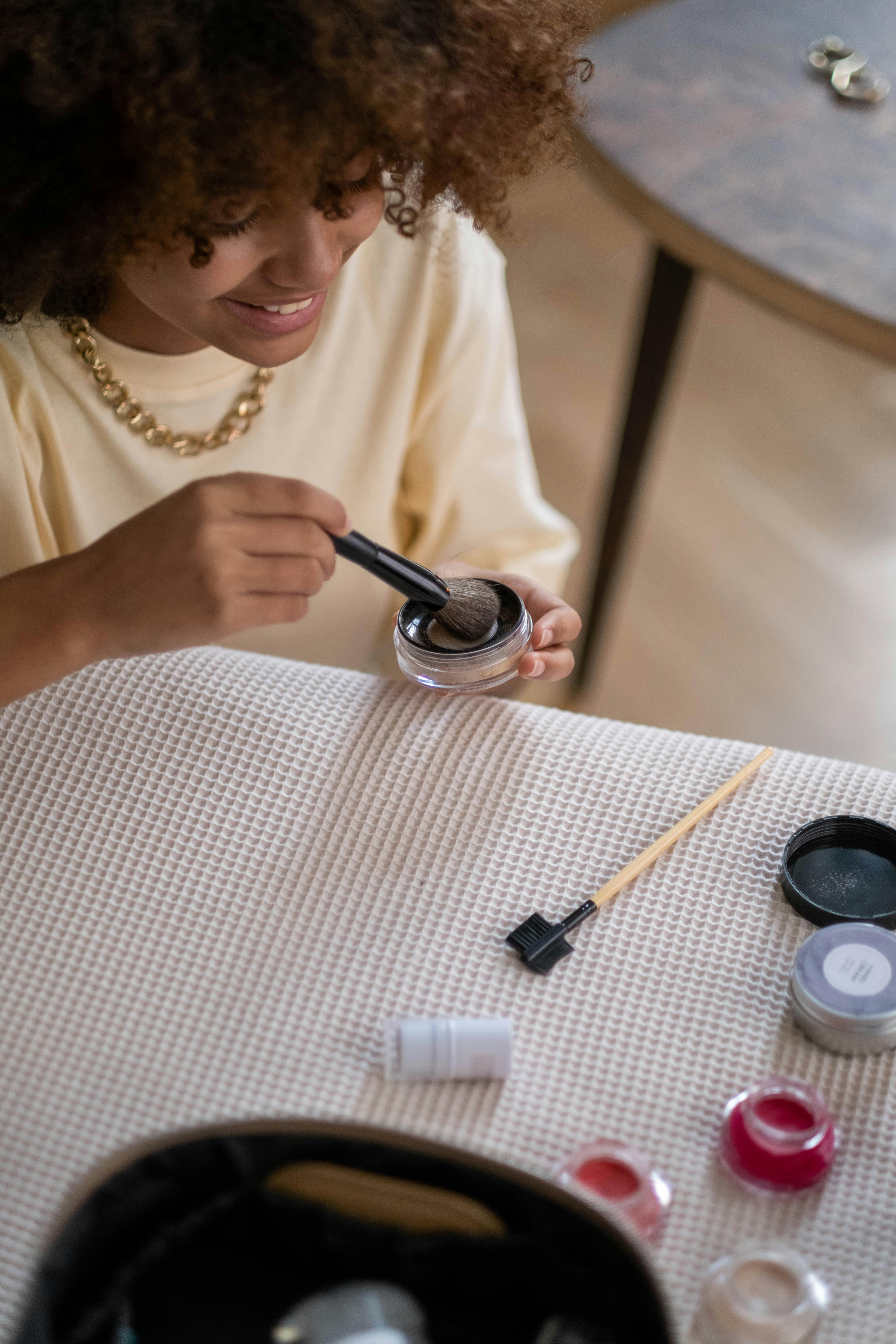 Free Happy woman with afro hair applying makeup in a relaxed indoor setting. Stock Photo