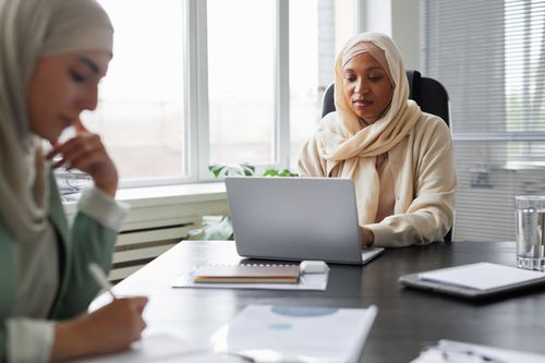 Free Two Muslim businesswomen working on laptops in a bright modern office setting. Stock Photo