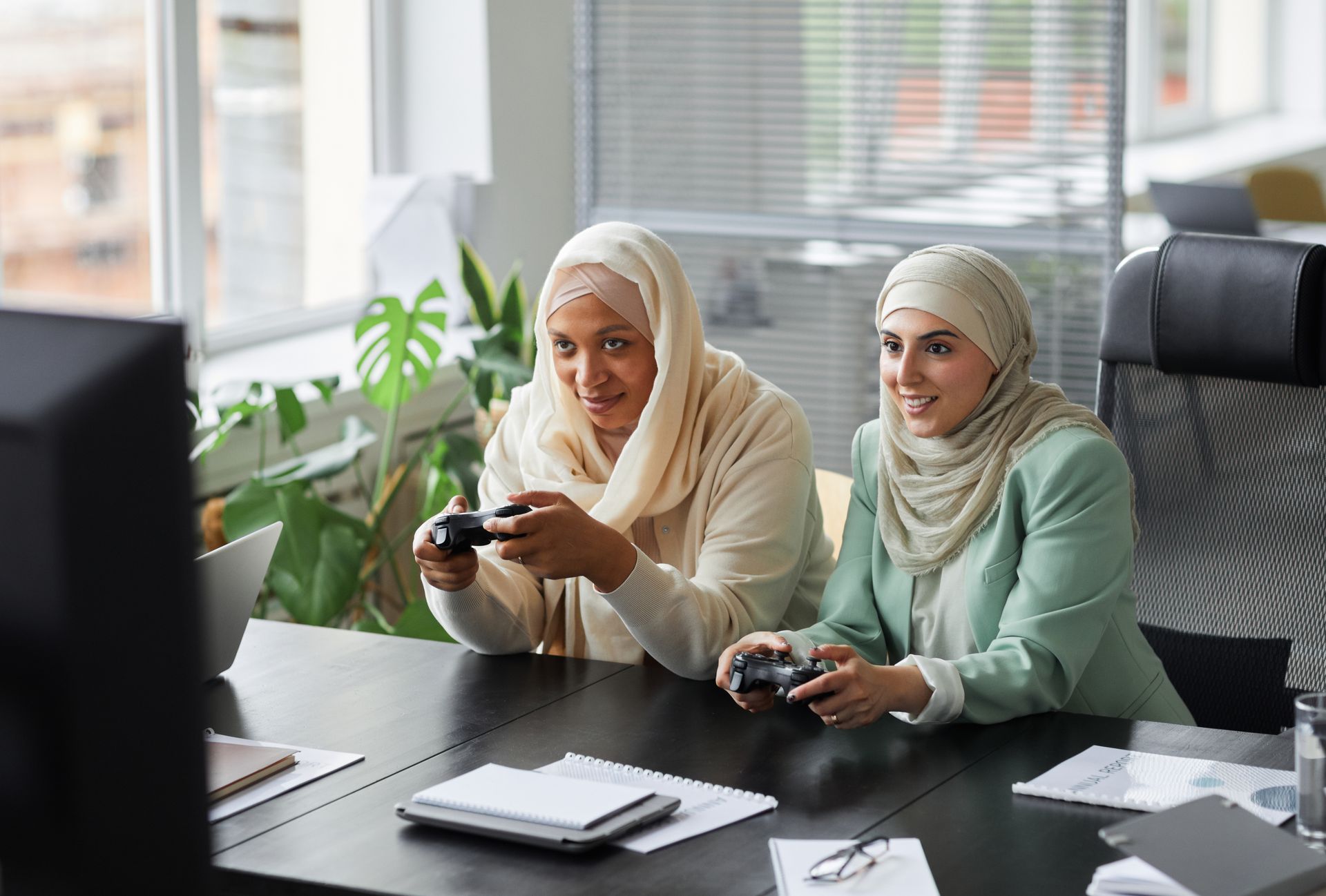 Two Muslim businesswomen enjoy gaming together during a break in a modern office.