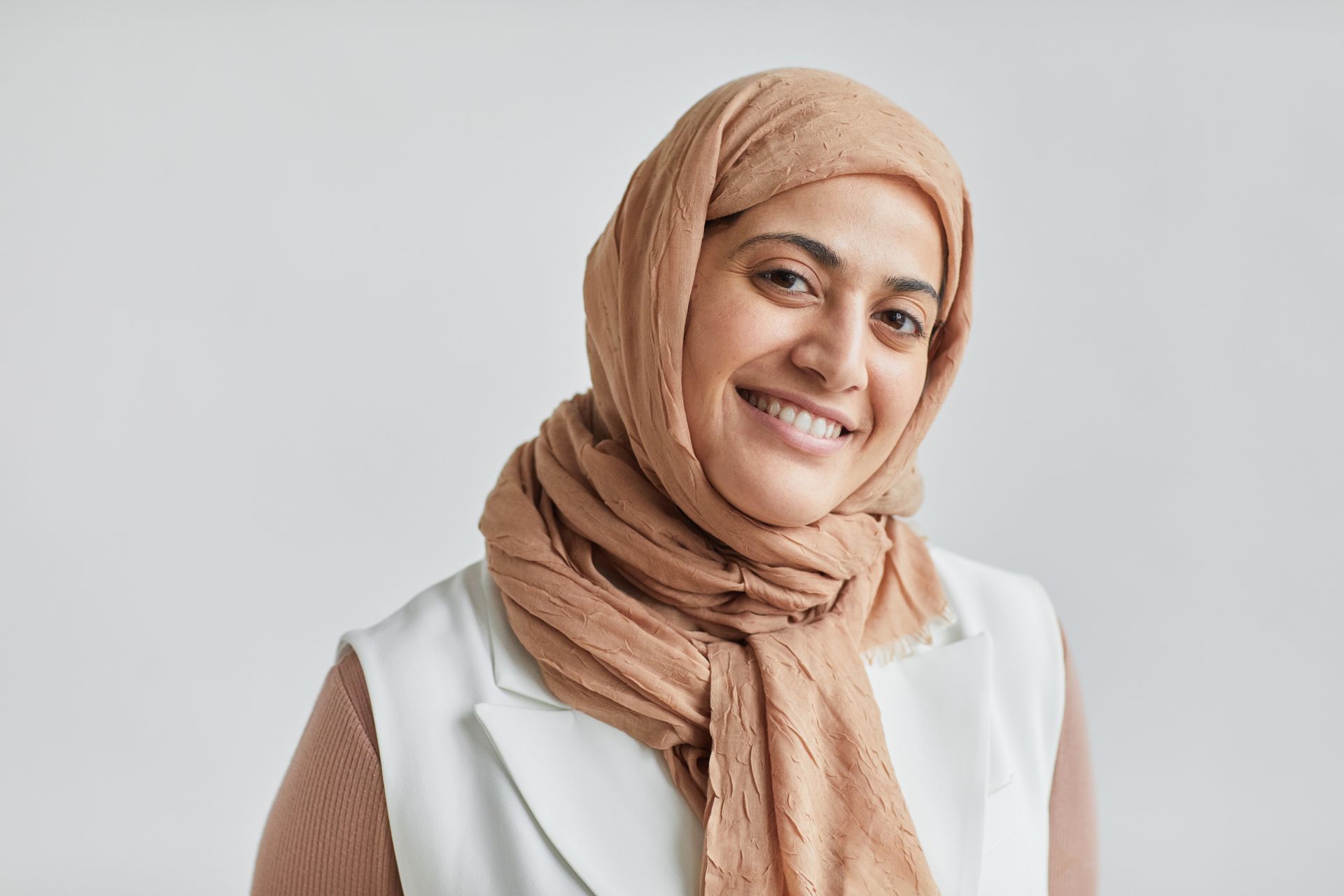 Portrait of a smiling Muslim woman in a hijab, wearing business attire.