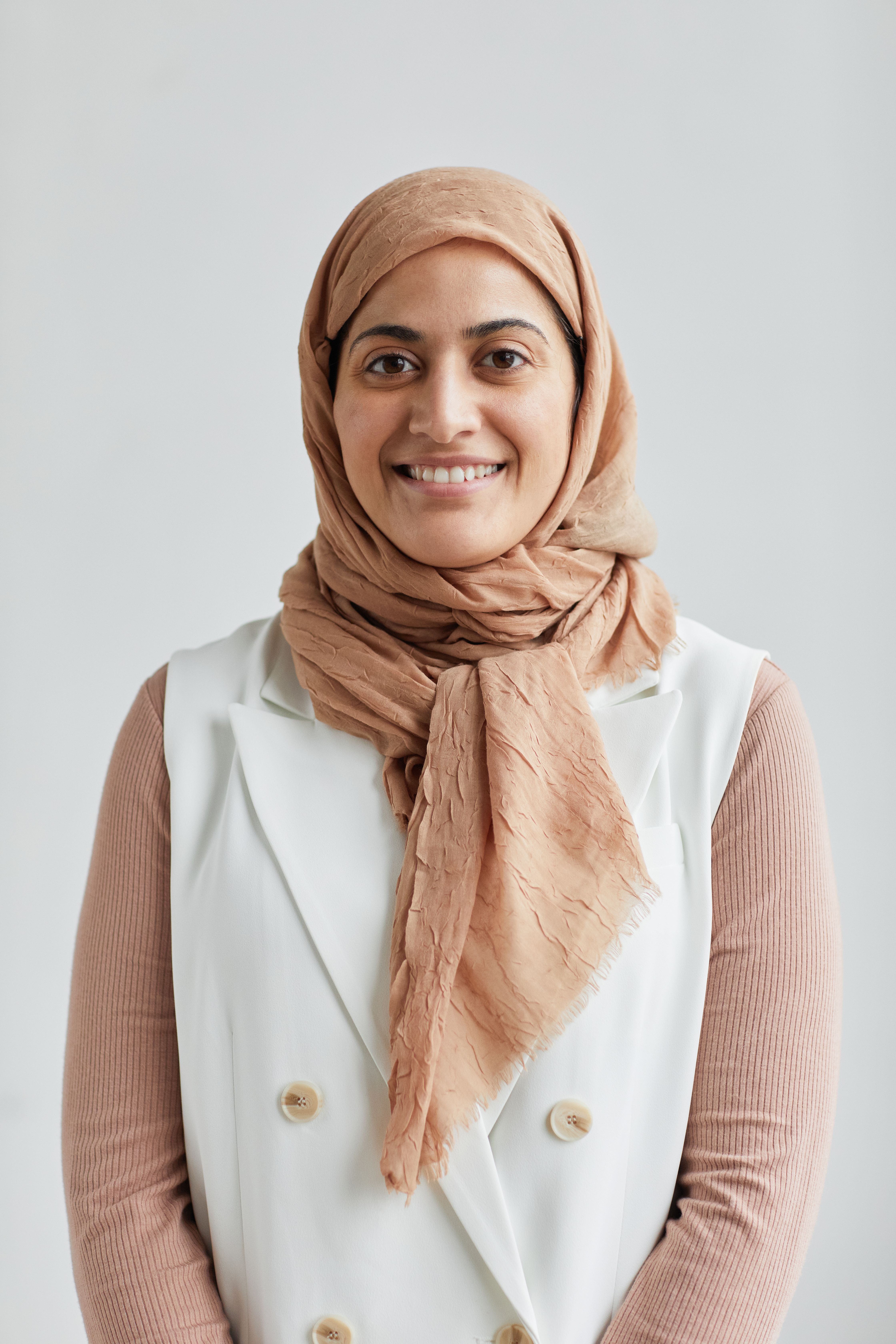 Studio portrait of a smiling woman in hijab against a white background, conveying warmth and positivity.