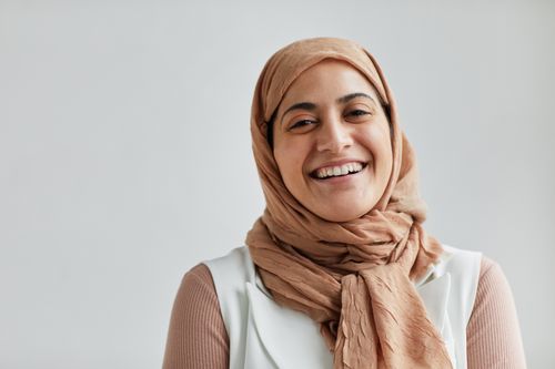Free A cheerful Muslim woman wearing a hijab smiles brightly against a white backdrop. Stock Photo