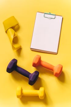 Vibrant fitness gear including dumbbells and a clipboard on a yellow backdrop.