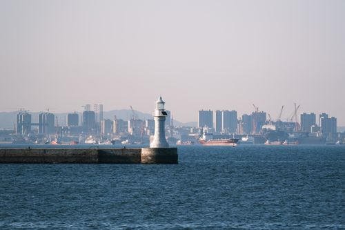 Free Scenic view of a lighthouse with urban city skyline backdrop over the ocean. Stock Photo