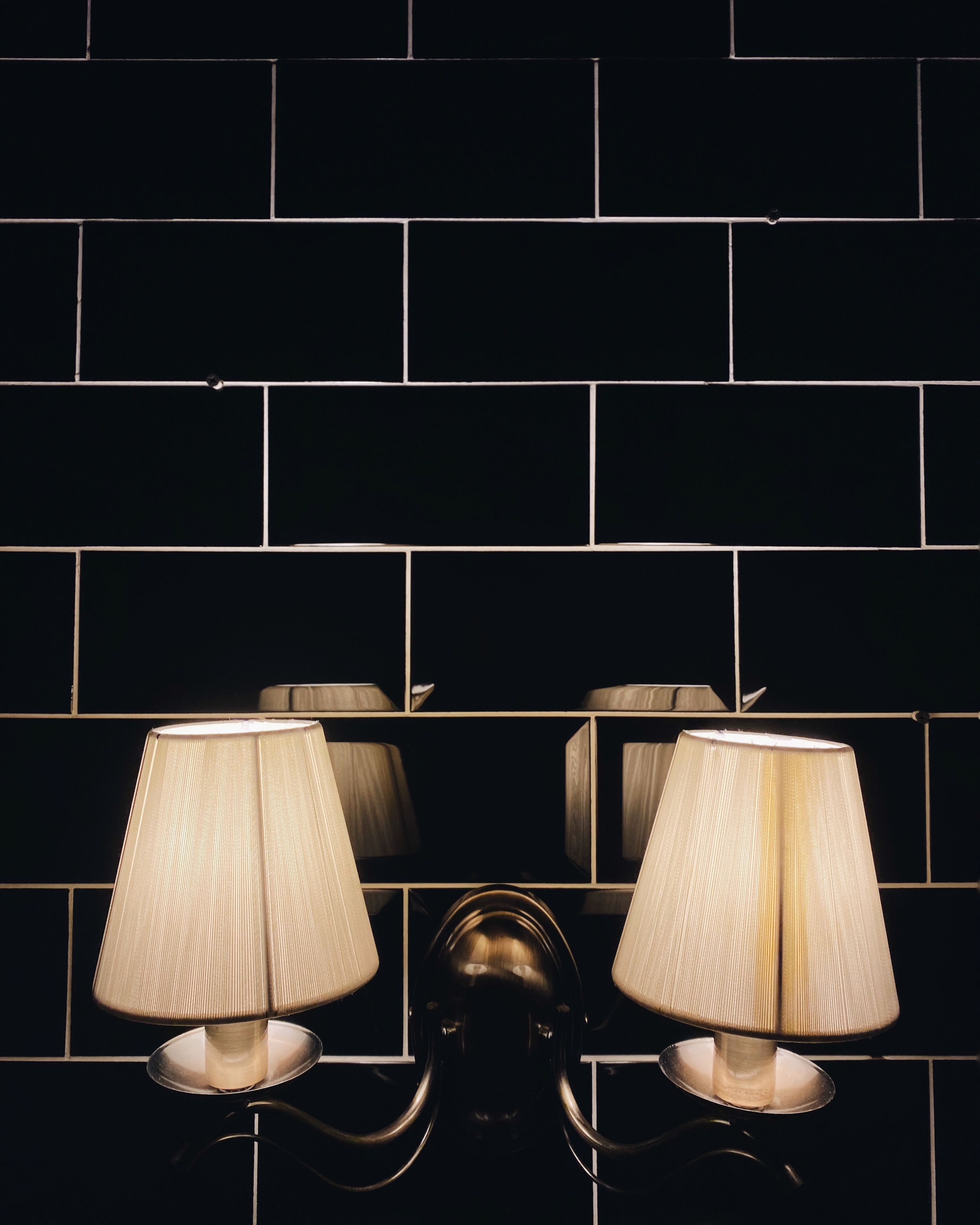 Dual lamps mounted on a black tiled wall create a warm ambiance with reflection effects.